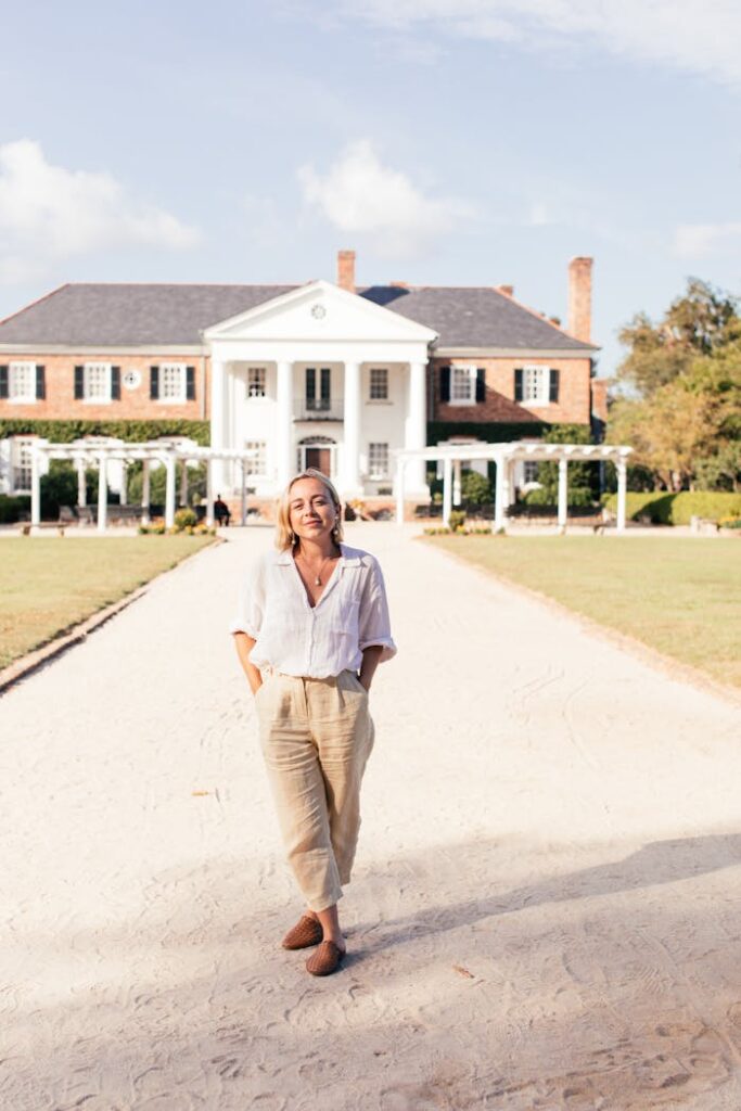 Woman walking on path leading to colonial-style mansion, exuding elegance and grace.